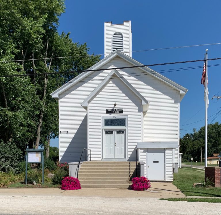 Village Hall, a white clapboard building with a bell tower, flagpole and flowers