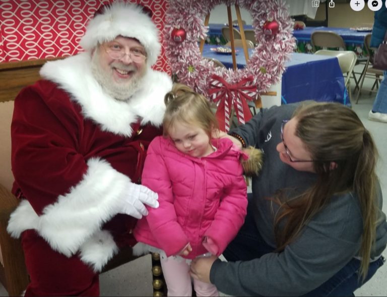 Santa Claus with a child and parent at the village holiday event