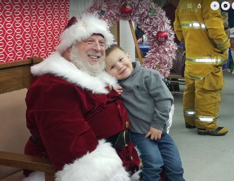 Santa Claus with a child, with a firefighter in gear nearby