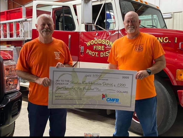 Two firefighters holding a donation check in front of a fire engine